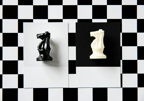 Zwarte en witte paarden op contrasterende velden in het schaakspel, die symbool staan voor strategie, rivaliteit en evenwichtige competitie.
