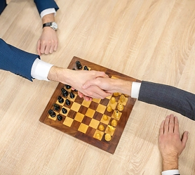 Twee spelers schudden elkaar de hand boven een schaakbord na een partij, een symbool van sportiviteit, respect en competitieve strategie in het klassieke bordspel schaken.