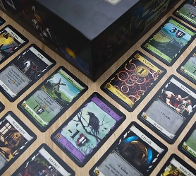 Een tafelspel met kaarten in fantasiethema, uitgespreid op een tafel naast een speldoos, die strategische kaartspellen voorstellen.